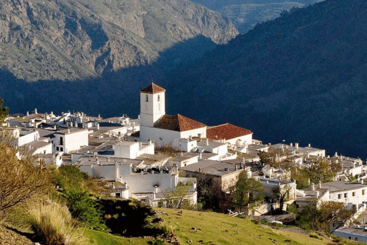 White village with a church in a mountainous landscape under sunlight.