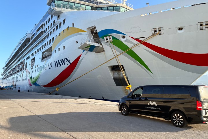 Docked cruise ship with colorful swirls and black van nearby.