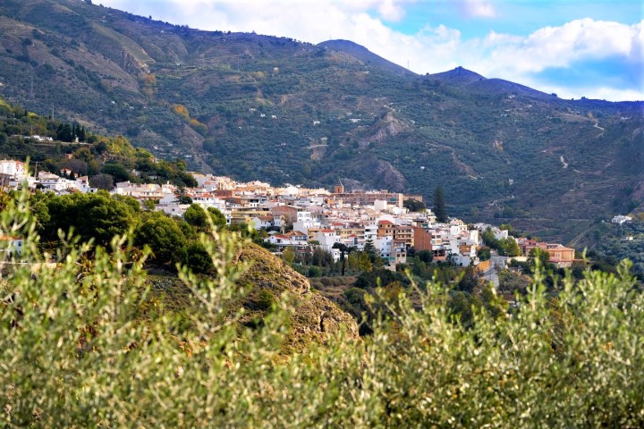 Hillside village with white buildings surrounded by green mountains under a blue sky.