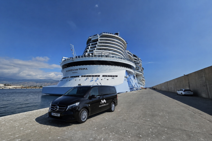 Large cruise ship docked by a concrete pier with a black van nearby.